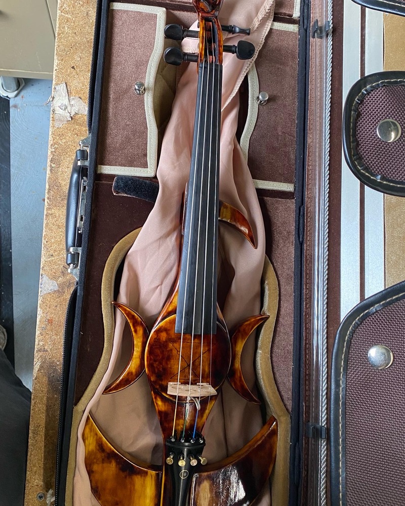 Electric violin featuring moon shaped components and a hand-shaped scroll