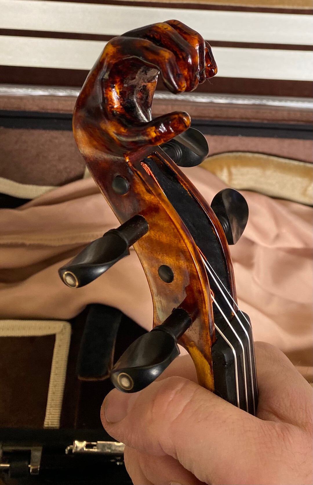 Image shows a violin pegbox terminating in a carved sculpture of a human hand instead of the usual nautilus spiral scroll