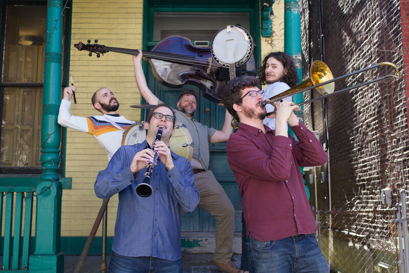 Five musicians on a green and yellow porch brandish their instruments at one another like weapons