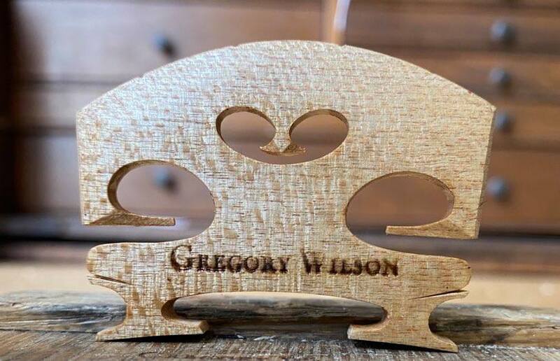 A hand carved viola bridge bearing a wood-burned brand reading 