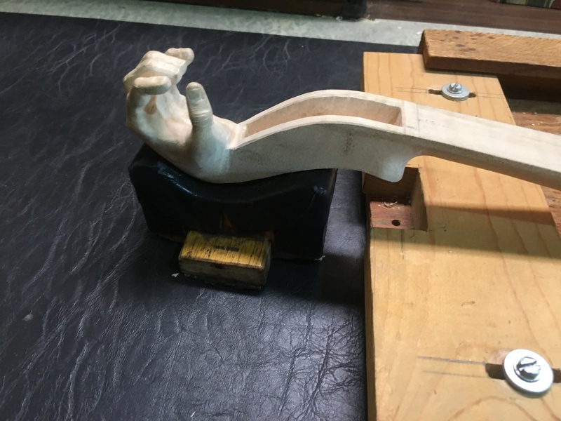 A closeup of a violin pegbox with a carved sculpture of a hand instead of the usual nautilus volute