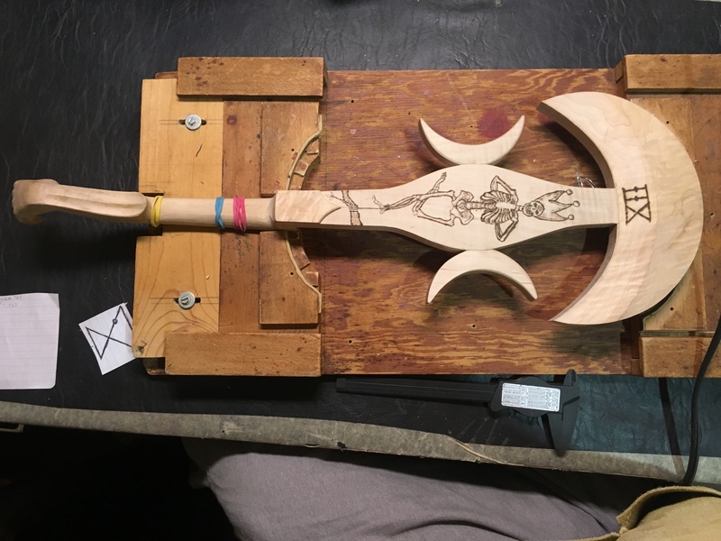 The back view of an electric violin featuring crescent moon shapes and a woodburned design of the 