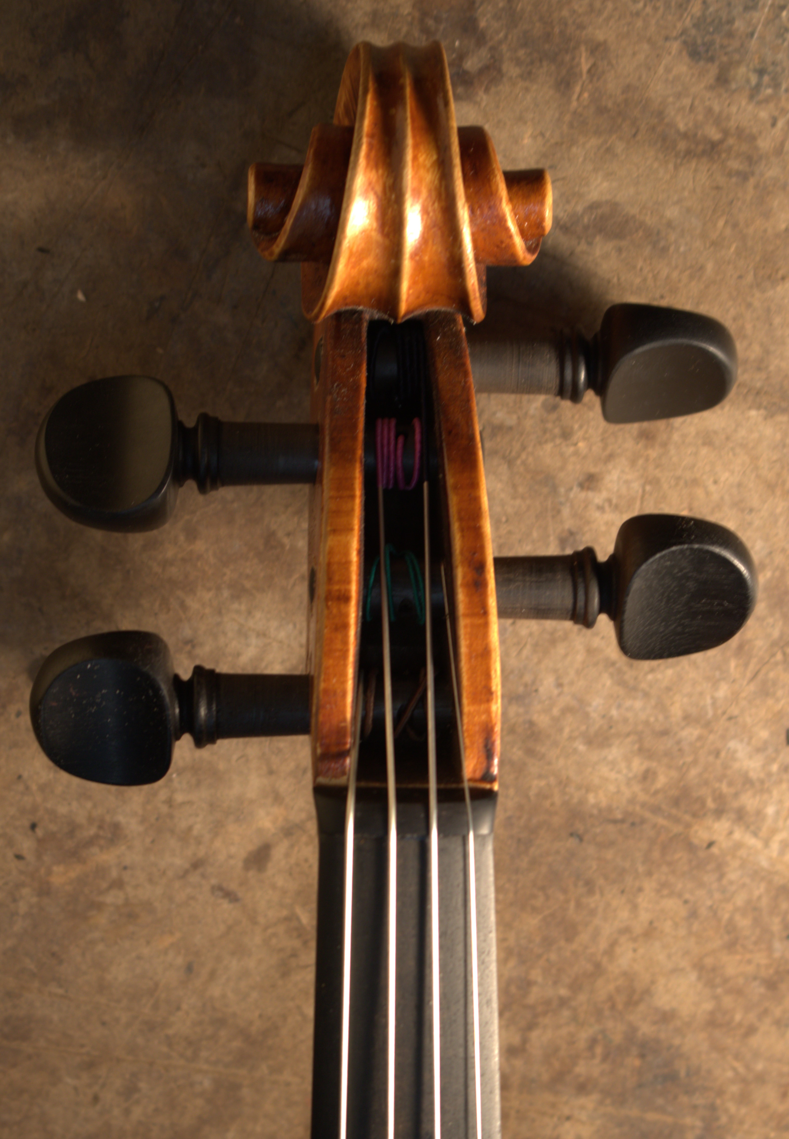 Image shows front view of a Guarneri del Gesu style violin scroll with orange-brown varnish and ebony tuning pegs